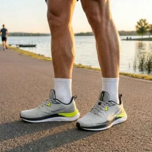 Close-up das pernas de um corredor usando o tênis Free Run cinza em uma pista de corrida à beira de um lago durante o pôr do sol.