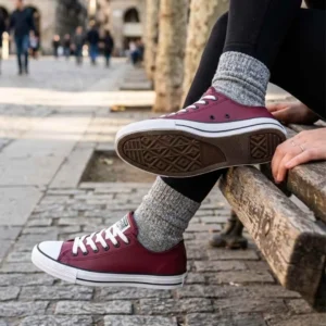 Tênis Feminino All Star Converse Couro. Detalhe lateral e do solado do Tênis All Star Converse Couro Bordo, com a pessoa sentada em um banco de madeira.