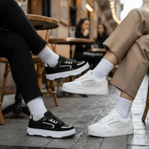 Tênis Feminino Casual Lisboa. Duas pessoas sentadas em um café externo usando diferentes modelos do Tênis Lisboa: um par inteiramente preto com detalhes brancos e outro par branco clássico.